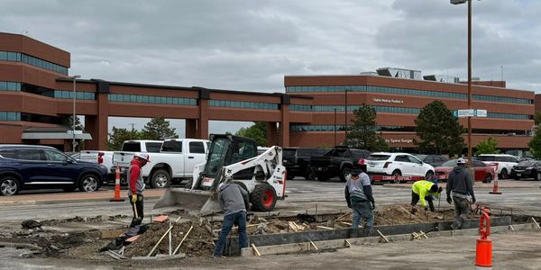 Construction workers operating machinery and preparing ground at a worksite near a hospital.
