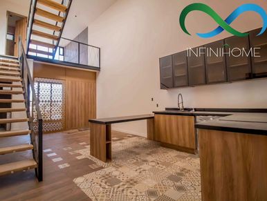 Modern kitchen with wooden cabinets and a staircase leading to a loft area.