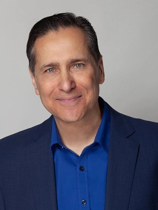 Man in blue shirt and jacket smiling at camera.
