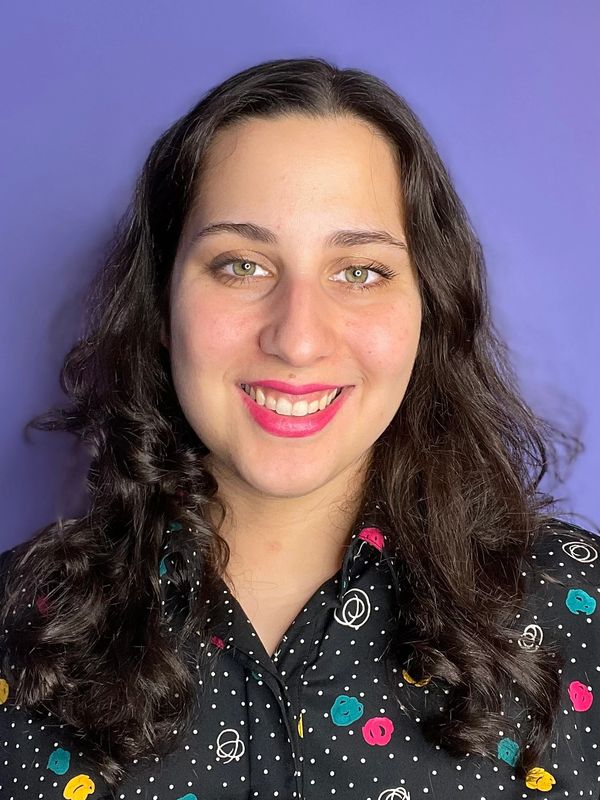 Smiling woman with curly dark hair against a purple background.