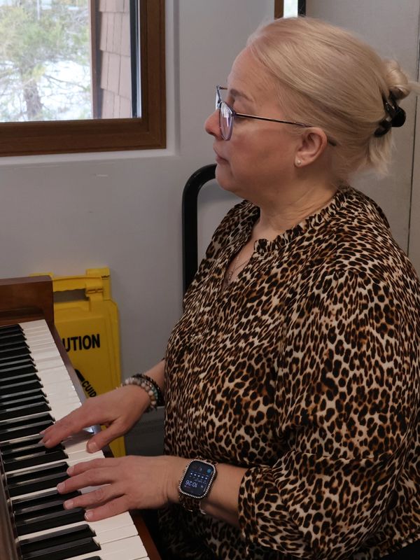Woman playing piano indoors near window.