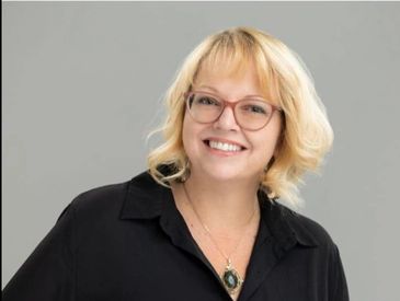 Smiling woman with blonde hair and glasses wearing a black shirt.