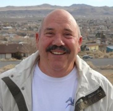 Smiling bald man with a mustache outdoors in a mountainous area.