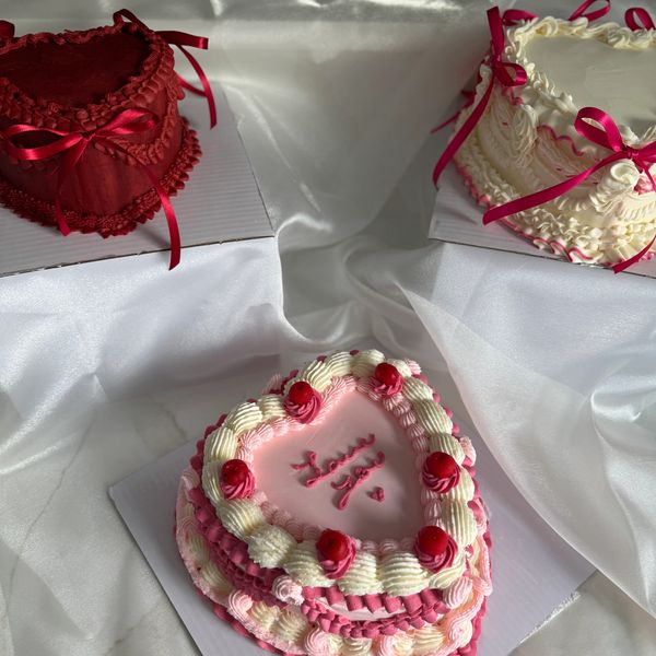 Three heart-shaped cakes decorated with cream and ribbons on a white cloth.