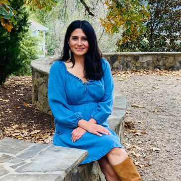 Woman in a blue dress sitting on a stone bench outdoors.