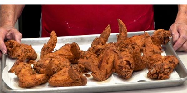 Tray of crispy fried chicken wings held by a person in a red shirt.