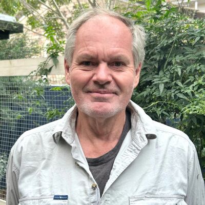 Smiling older man standing outdoors near greenery.