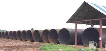 Large steel pipes lined up outdoors near a metal shed.