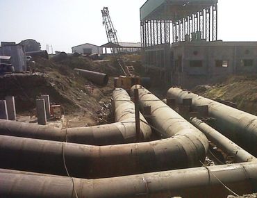 Large industrial pipes and a crane at a construction site.