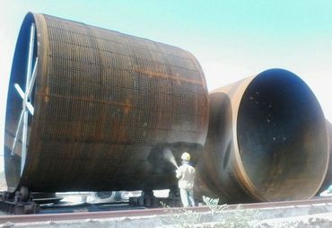 Worker cleaning large industrial metal cylinders outdoors.