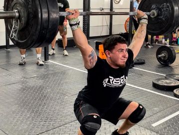 Man performing a heavy barbell overhead squat in a gym setting.
