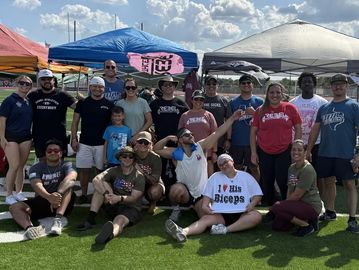 Group of people posing together outdoors under tents on a sunny day.