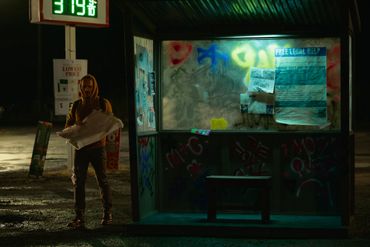 Person holding an umbrella at a dimly lit bus stop covered in graffiti.