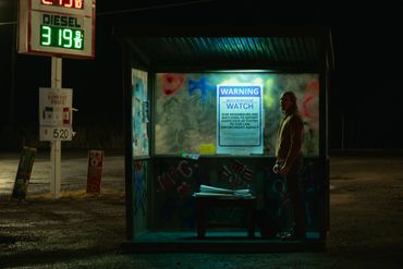 A man stands inside a dimly lit, graffiti-covered bus stop at night.
