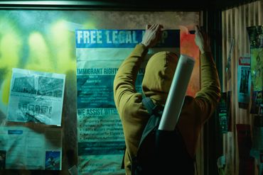 Person in hoodie posting a 'Free Legal Help' immigrant rights flyer on a wall at night.