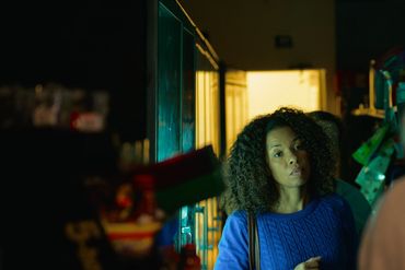 Woman in blue sweater holding a bottle in a dimly lit store.