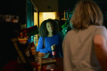 Woman in blue sweater holding a bottle in a dimly lit store.