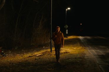 Person walking alone at night on a dimly lit road.
