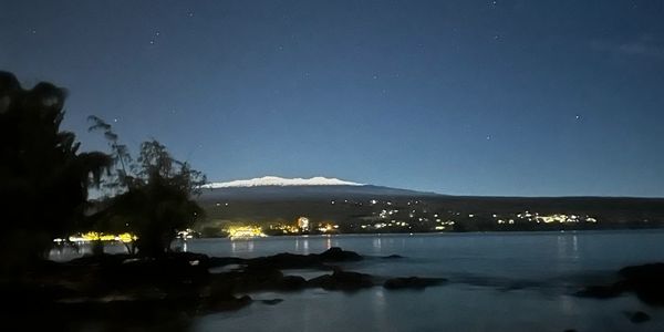 Night view of a coastal town with a snow-capped mountain in the background.