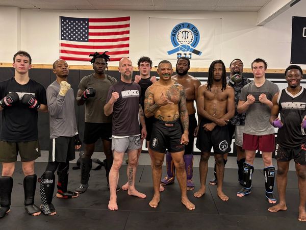 Group of fighters posing in a gym with American flag behind them.