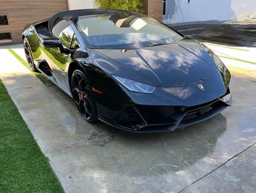 Black Lamborghini convertible parked on a driveway with reflections on its surface.