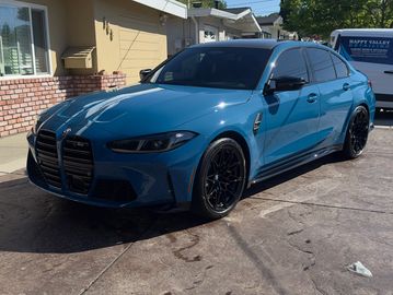 A sleek blue BMW sedan parked in a driveway under sunlight.