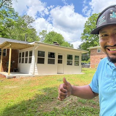Man smiling and giving thumbs up in front of a small white house.
