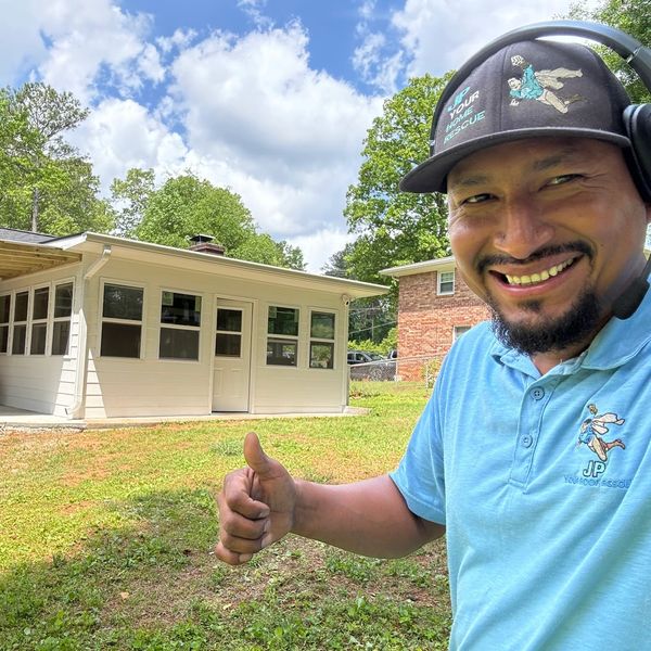 Man giving thumbs up in front of a house under blue sky.