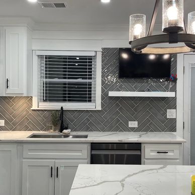 Modern kitchen with white cabinets and gray herringbone backsplash.