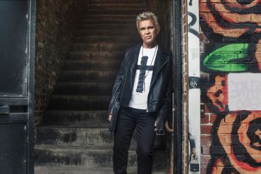 Man in leather jacket standing by stairway with graffiti.