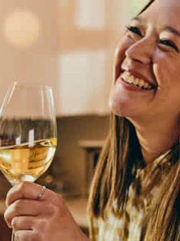 A woman happily holding a glass of white wine.