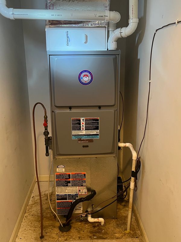 A furnace unit installed in a small utility space with pipes and warning labels.