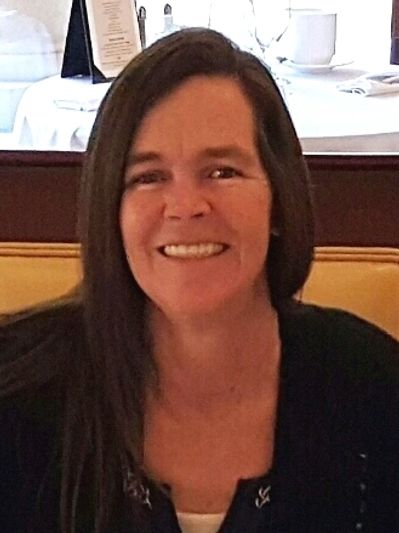 Smiling woman with long dark hair sitting indoors at a restaurant.