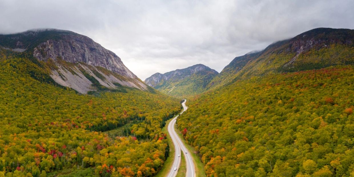 A winding road through a colorful autumn forest between mountains.