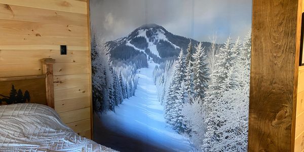 Cozy bedroom with snowy mountain mural and wooden walls.