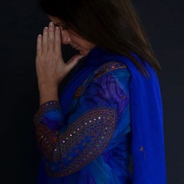 Woman in blue traditional attire with hands clasped in prayer.