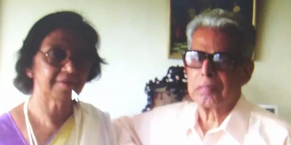 Elderly couple posing indoors, both wearing glasses.