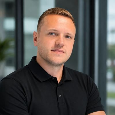 Porträt eines Mannes im schwarzen Polohemd mit verschränkten Armen.
