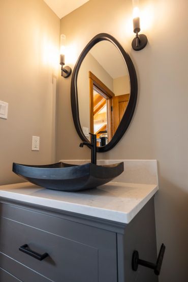 Modern bathroom vanity with black vessel sink and oval mirror.