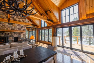 Cozy wooden cabin living room with large windows and a stone fireplace.