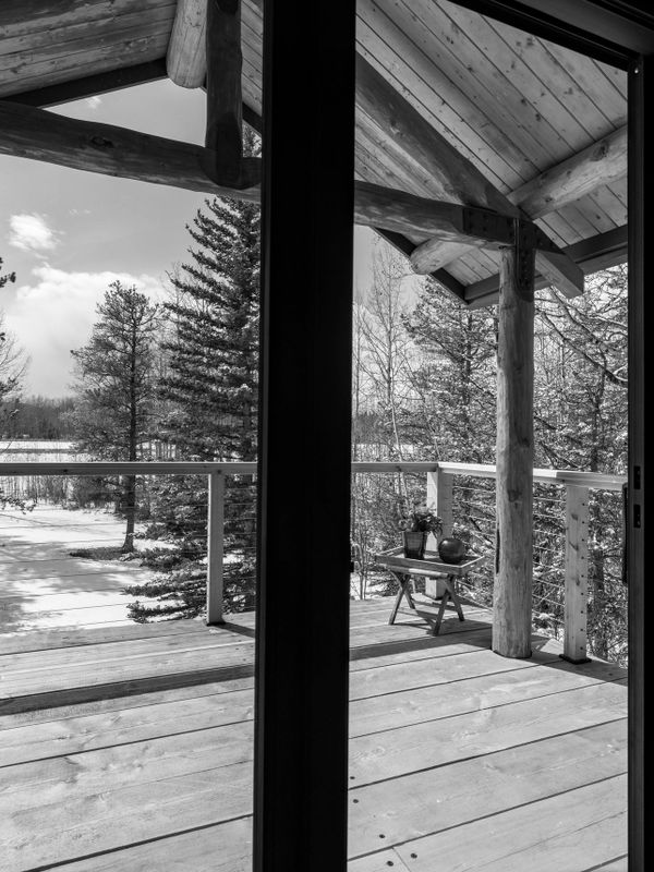 View of a wooden deck and snowy forest through a glass door.