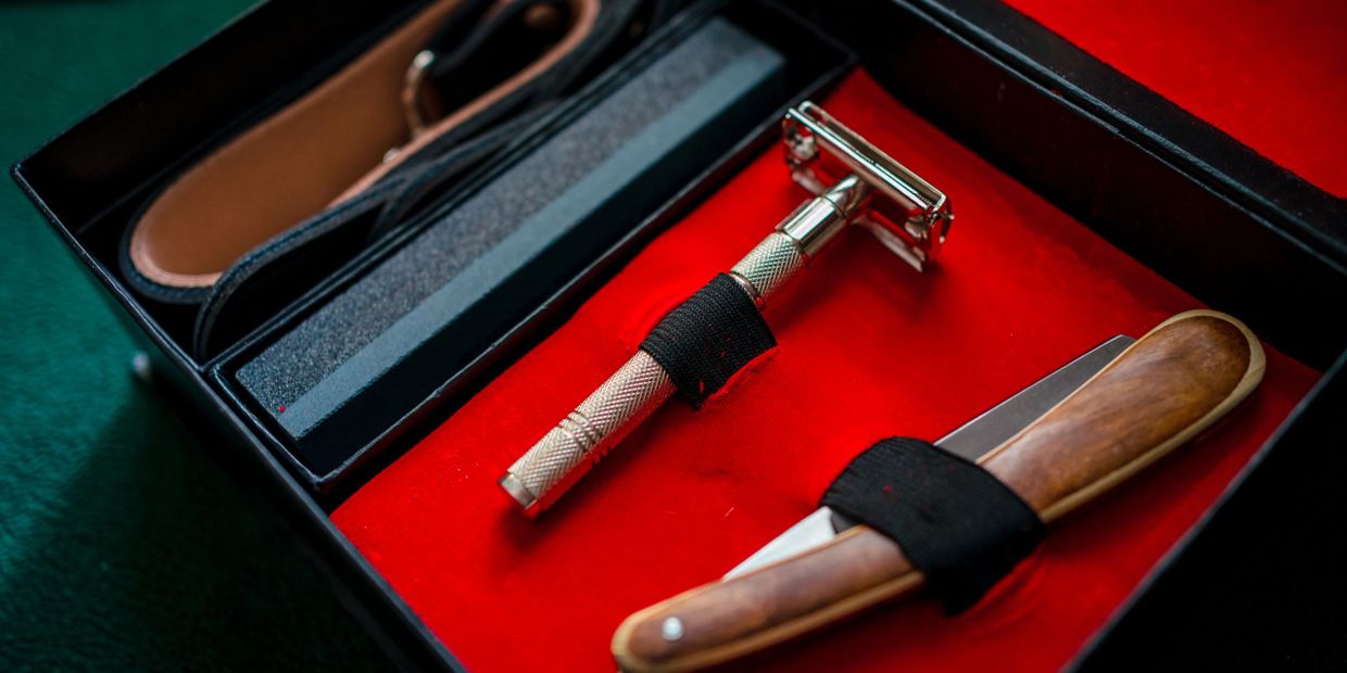 A shaving kit with a razor and a wooden-handled straight razor on red velvet.
