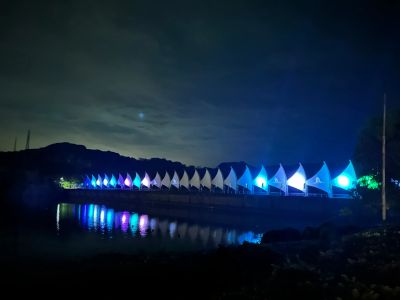 Illuminated sails glowing blue and white reflected on calm water at night.