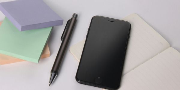 Smartphone, pen, sticky notes, and notebook on a desk.
