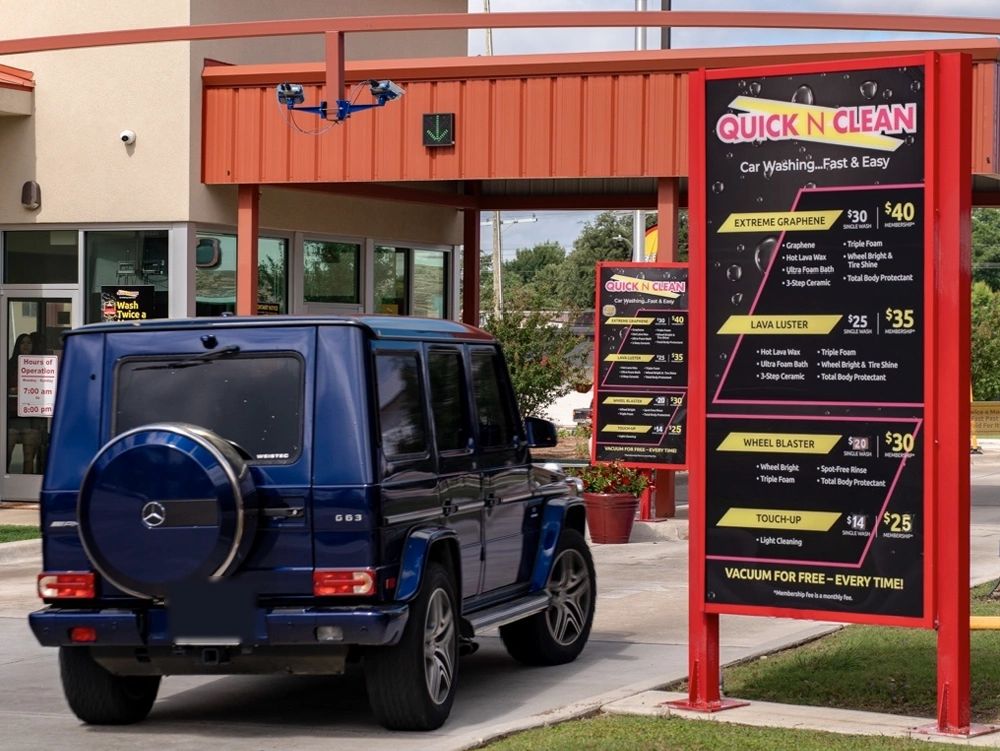 Luxury SUV at car wash drive-thru with pricing sign.