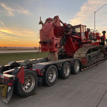 Large red construction vehicle loaded on a trailer at sunset.