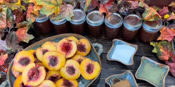 Fresh peaches, spices, and jars of homemade preserves with autumn leaves decoration.