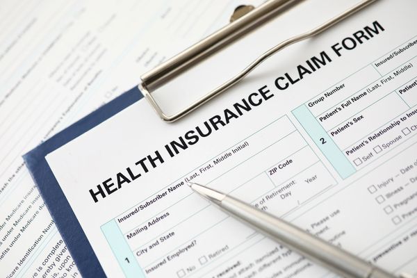 A silver pen rests on a clipboard with a "HEALTH INSURANCE CLAIM FORM".