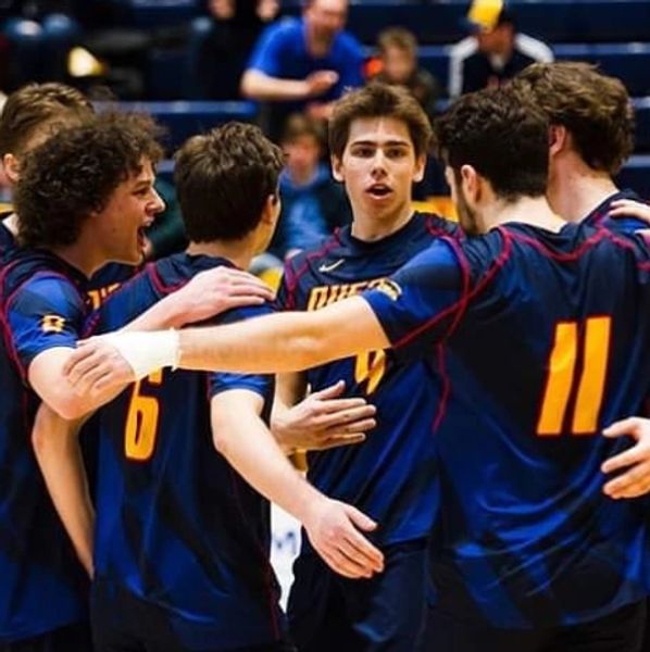 Group of men's volleyball players rally after a point is scored.