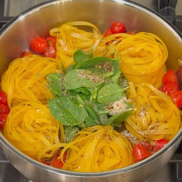 Uncooked pasta nests with spinach and cherry tomatoes in a pot with seasoning.